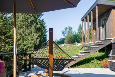 Çağdaş bir eve giden hamak, teras şemsiyesi ve ahşap merdivenlerle çevrili modern bir açık alan..