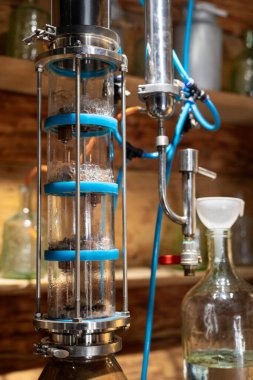 Cam bileşenleri ve mavi aksanlı laboratuvar damıtma aparatı. Kurulum bir yoğunlaştırıcı ve kimyasal işlemler için çeşitli cam kaplar içerir.