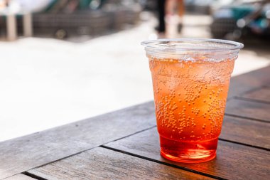 Portakallı sodayla dolu şeffaf plastik bir bardakta ferahlatıcı bir alkol. Kokteyl bardağı, arka planda bulanıklık olan ahşap bir masaya konur..