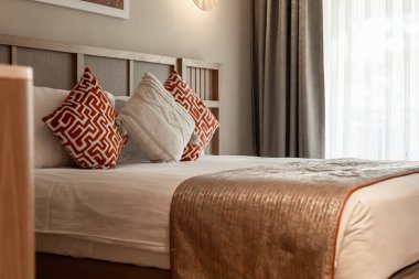 Dekoratif yastıklı, düzgünce yapılmış bir yatak odası. Yumuşak ışıklandırma ve perdeler lüks otel odasında sıcak bir atmosfer yaratır.