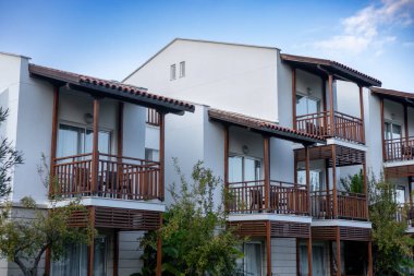 Bulutlu bir gökyüzünün altında sakin bir göletin yakınındaki palmiye ağaçları ve yeşilliklerle çevrili modern otel binası