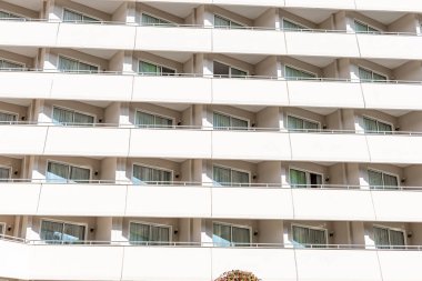 Çoklu balkonları ve geniş pencereleri olan modern bir otel binası. Bina temiz, beyaz bir görünüme sahip ve çevresi yeşillikle çevrili..