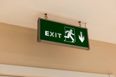 Yeşil çıkış işareti, çalışan bir figür ve aşağı doğru ok. Tabela duvara asılmış, çıkış yönünü gösteriyor.
