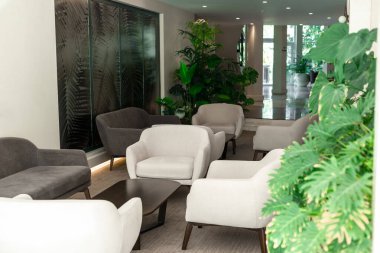 İki modern gri sandalye ve arka planda yemyeşil bitkiler olan şık bir iç mekânda küçük bir masa.