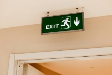 Yeşil çıkış işareti, çalışan bir figür ve aşağı doğru ok. Tabela duvara asılmış, çıkış yönünü gösteriyor.