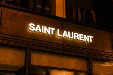 Viyana, Avusturya - 15 Aralık 2025: Avusturya 'nın Viyana kentinde dokulu bir duvarda aydınlatılmış YSL logosu. Logo belirgin bir şekilde gösteriliyor, markaların ikonik tasarımı sergileniyor.