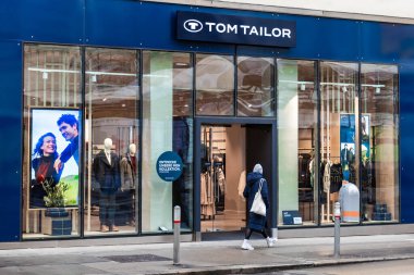 Viyana, Avusturya - 15 Aralık 2025: Viyana, Avusturya 'da Tom Tailor' un bir mağazası. Mağazada giysi gösteren büyük cam pencereler yer alıyor. İnsanlar alışveriş faaliyetleriyle meşgul olarak buradan geçiyorlar..