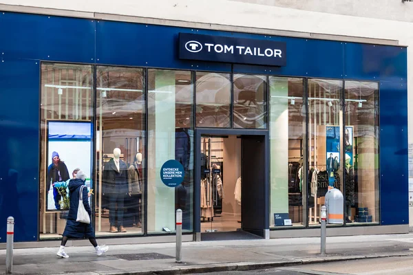 Viyana, Avusturya - 15 Aralık 2025: Viyana, Avusturya 'da Tom Tailor' un bir mağazası. Mağazada giysi gösteren büyük cam pencereler yer alıyor. İnsanlar alışveriş faaliyetleriyle meşgul olarak buradan geçiyorlar..
