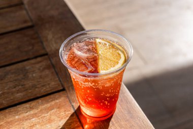 Portakallı sodayla dolu şeffaf plastik bir bardakta ferahlatıcı bir alkol. Kokteyl bardağı, arka planda bulanıklık olan ahşap bir masaya konur..