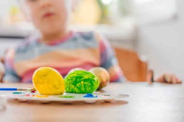 Renkli Paskalya sarısı ve yeşil yumurtalar odak noktasında. Tavşan kulaklı bulanık çocuk. Bayram kutlaması ve bahar aile geleneği. Yüksek kalite fotoğraf