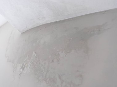 Açık gri bir yüzeyi ve beyaz bir köşesi olan dokulu bir duvarın yakından görüntüsü. Duvarda aşınma ve dengesizlik belirtileri var.