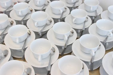 Masada bir sürü boş porselen bardak var. Beyaz, düzgün ve kaşıklarıyla güzelce dizilmişler..