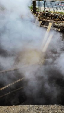 Tamir ya da acil durum alanındaki derin bir çukurdan yoğun bir buhar / duman sütunu yükseliyor. Arka planda tahta destekler ve metal eskrim görülebiliyor.