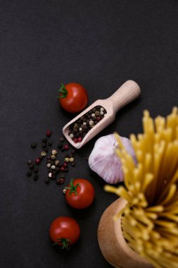 Çiğ makarna, taze vişneli domates, sarımsak ve koyu arkaplanda karışık biberli mısır baharatları. İtalyan mutfağı konsepti, yemek malzemeleri, yemek hazırlama, sade mutfak....