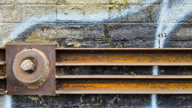 Duvara yapışmış paslı çelik bir kirişin yakın çekimi ve grafiti izleri. Yapı, yıkım, yaşlanma materyalleri ve endüstriyel geçmiş kavramlarını gösteren endüstriyel bir kentsel doku..