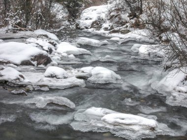 Kış ormanlarında donmuş nehir ve kardaki taşlar.