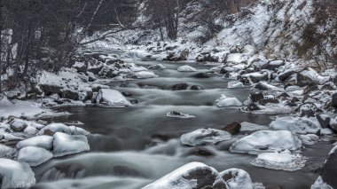 Karda kayalık bir dağın içinden akan bir nehrin dikey görüntüsü.