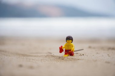 Plajda yürüyen küçük bir cankurtaran figürü. Elinde bulanık arka planı olan dürbünler var.