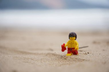 Plajda yürüyen küçük bir cankurtaran figürü. Elinde bulanık arka planı olan dürbünler var.