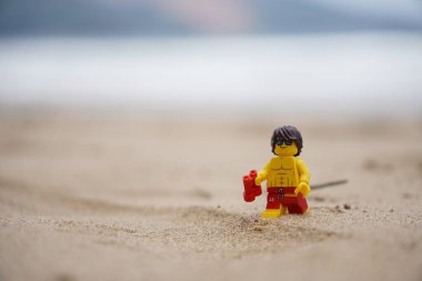 Plajda yürüyen küçük bir cankurtaran figürü. Elinde bulanık arka planı olan dürbünler var.