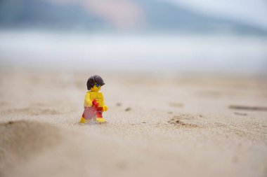 Plajda yürüyen küçük bir cankurtaran figürü. Elinde bulanık arka planı olan dürbünler var.