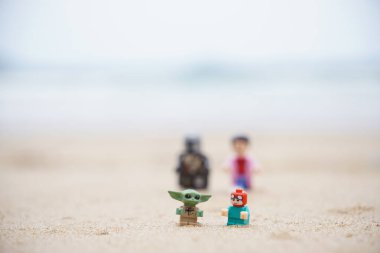 Gündüzleri sahilde oynayan çocuklarına bakan iki babayı betimleyen 4 Lego minyatür figürü..