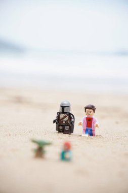 Gündüzleri sahilde oynayan çocuklarına bakan iki babayı betimleyen 4 Lego minyatür figürü..