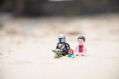 Gündüzleri sahilde oynayan çocuklarına bakan iki babayı betimleyen 4 Lego minyatür figürü..