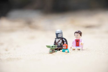 Gündüzleri sahilde oynayan çocuklarına bakan iki babayı betimleyen 4 Lego minyatür figürü..