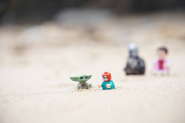 Gündüzleri sahilde oynayan çocuklarına bakan iki babayı betimleyen 4 Lego minyatür figürü..