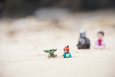 Gündüzleri sahilde oynayan çocuklarına bakan iki babayı betimleyen 4 Lego minyatür figürü..