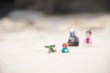 Gündüzleri sahilde oynayan çocuklarına bakan iki babayı betimleyen 4 Lego minyatür figürü..
