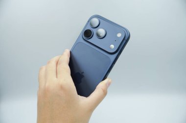 iPhone 17 'nin arkasını gösteren bir el. 3 kameralı derin mavi varyant.