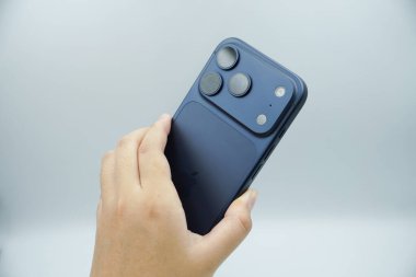 iPhone 17 'nin arkasını gösteren bir el. 3 kameralı derin mavi varyant.