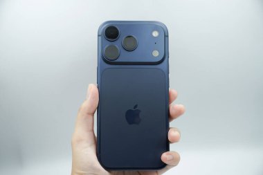 iPhone 17 'nin arkasını gösteren bir el. 3 kameralı derin mavi varyant.