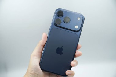 iPhone 17 'nin arkasını gösteren bir el. 3 kameralı derin mavi varyant.