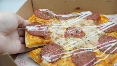 Bir el pizza kutusundan sosis ve mozzarella peynirli bir dilim pizza alıyor.