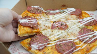 Bir el pizza kutusundan sosis ve mozzarella peynirli bir dilim pizza alıyor.