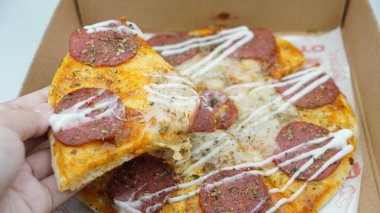 Bir el pizza kutusundan sosis ve mozzarella peynirli bir dilim pizza alıyor.