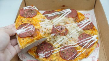 Bir el pizza kutusundan sosis ve mozzarella peynirli bir dilim pizza alıyor.