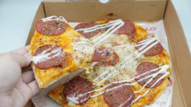 Bir el pizza kutusundan sosis ve mozzarella peynirli bir dilim pizza alıyor.