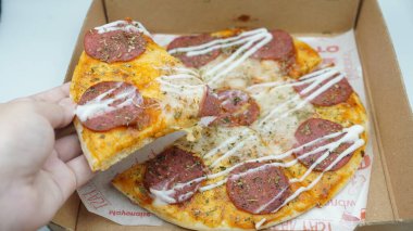 Bir el pizza kutusundan sosis ve mozzarella peynirli bir dilim pizza alıyor.