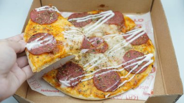 Bir el pizza kutusundan sosis ve mozzarella peynirli bir dilim pizza alıyor.