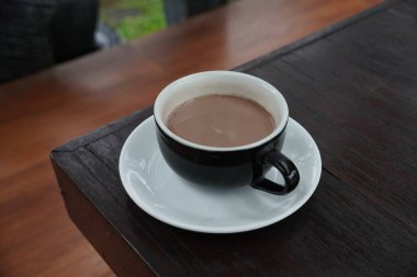 Bir fincan sıcak çikolata siyah bir fincanda ve siyah bir ahşap masada servis edilir..