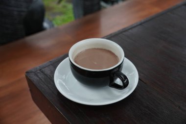 Bir fincan sıcak çikolata siyah bir fincanda ve siyah bir ahşap masada servis edilir..