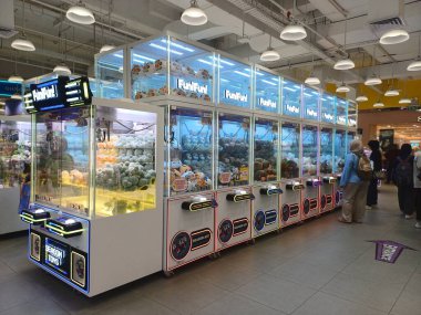 Alışveriş merkezinin içindeki bir oyun salonunda birkaç kişi tarafından oynanan pençe makineleri.