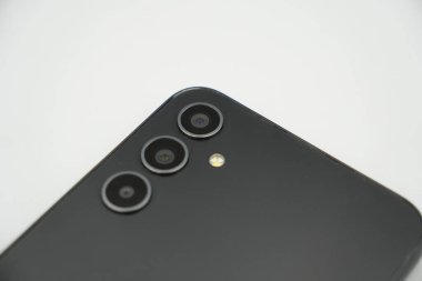 Üç kamera siyah bir akıllı telefona bağlanıyor. Flaşlı ve beyaz bir arkaplanı var..