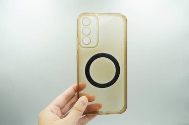 Bir el, ortasında manyetik bir halka olan açık sarı bir çantayı tutar..