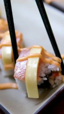 Suşi rulosunu krem peynir kapağıyla plastik tepsi kapağından ahşap çubuklarla alıyorum. Geleneksel Asya yemekleri. Sağlıklı doğu deniz ürünleri. Yüksek kalite 4k görüntü