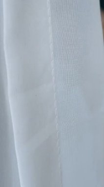 Yatak odasındaki sandalyede oturan, eline krem sürerek gülümseyen, bornozlu, zarif, olgun, sarışın bir kadın. Yumuşak güneş ışığı perdeden geçer.